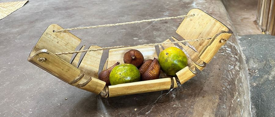 A curved bamboo fruit bowl shaped like an armadillo, holding limes and snake fruit