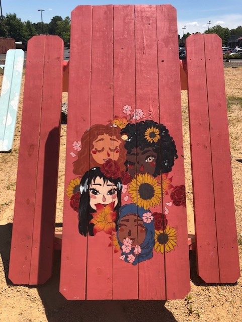 A picnic table hand-painted with four women among sunflowers and roses